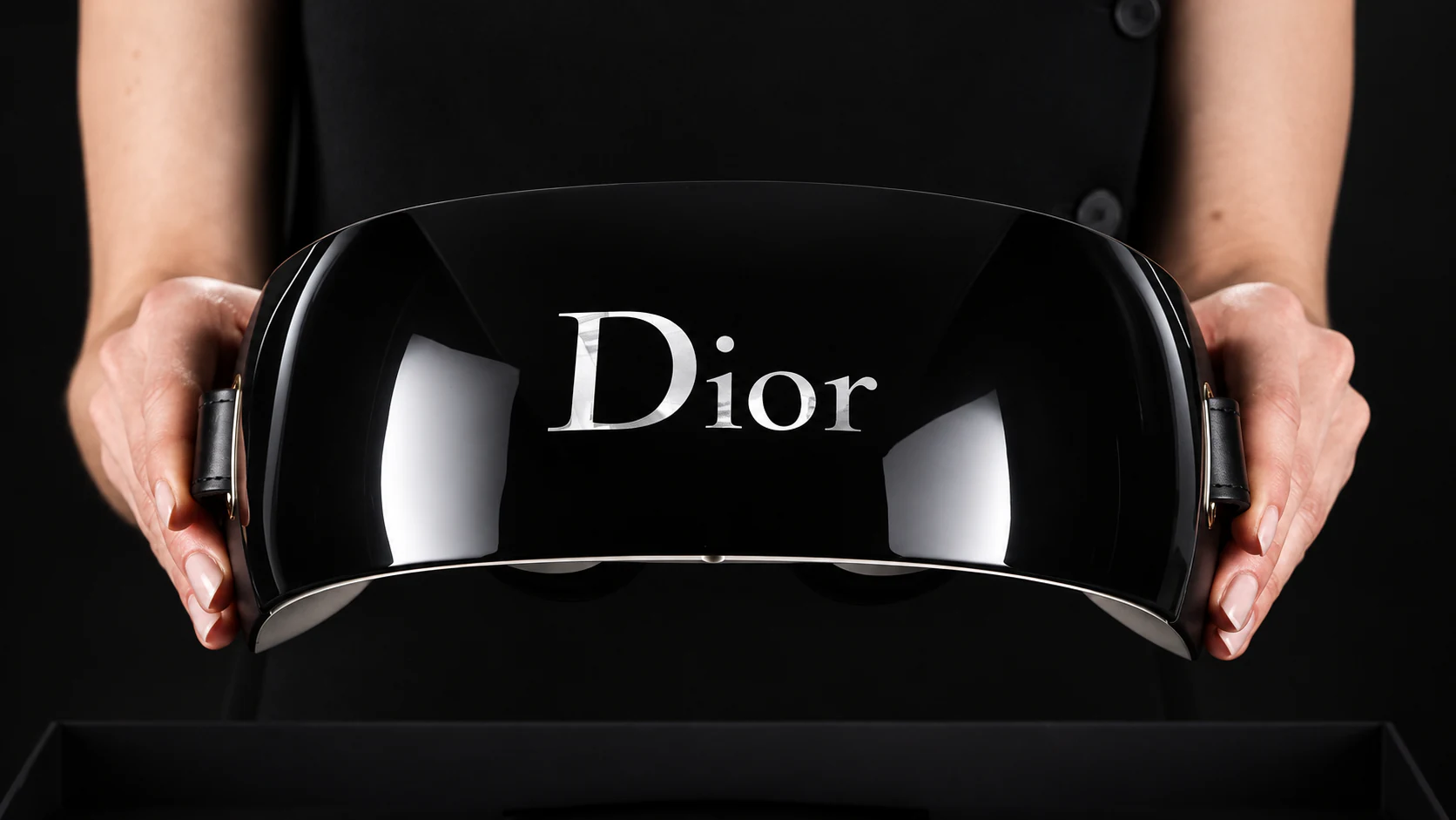 Hands presenting the glossy black Dior Eyes virtual reality headset